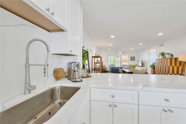 kitchen featuring visible vents, a sink, white cabinetry, and light stone countertops