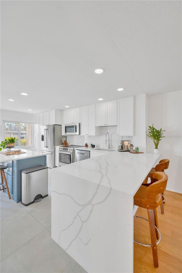 1600 1st Ave W Unit 102A, Bradenton, FL 34205 - kitchen with stainless steel appliances, white cabinets, a kitchen bar, light stone countertops, and recessed lighting