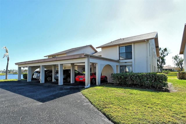 view of front facade featuring a water view, stucco siding, covered parking, and a front yard