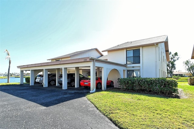 view of front of home featuring covered parking, a front yard, a water view, and stucco siding