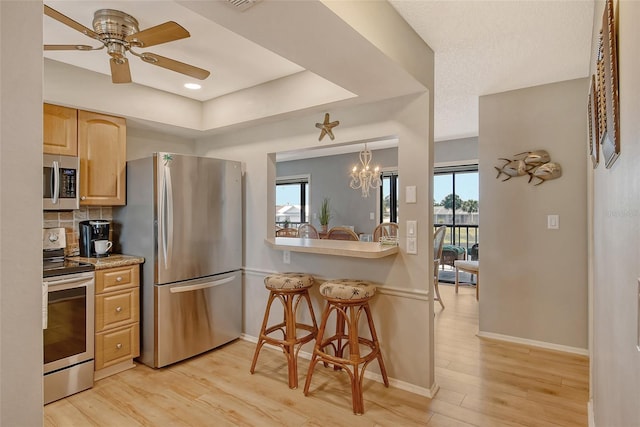 kitchen with appliances with stainless steel finishes, a healthy amount of sunlight, backsplash, and light wood finished floors