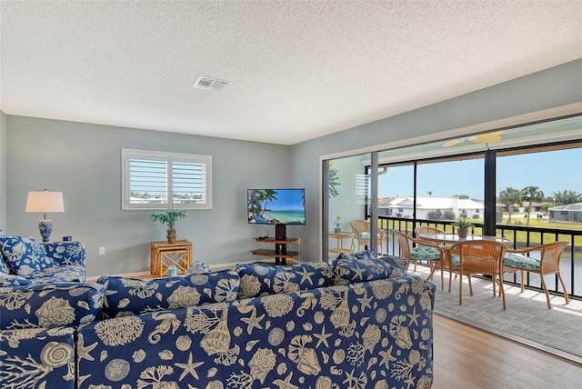 living room with a textured ceiling, plenty of natural light, wood finished floors, and visible vents