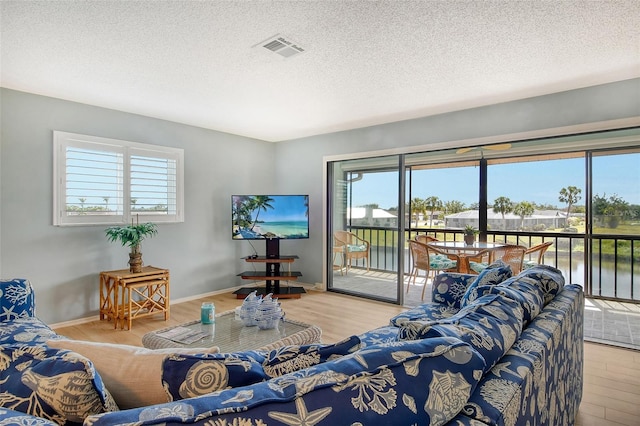 living area featuring baseboards, a textured ceiling, visible vents, and wood finished floors