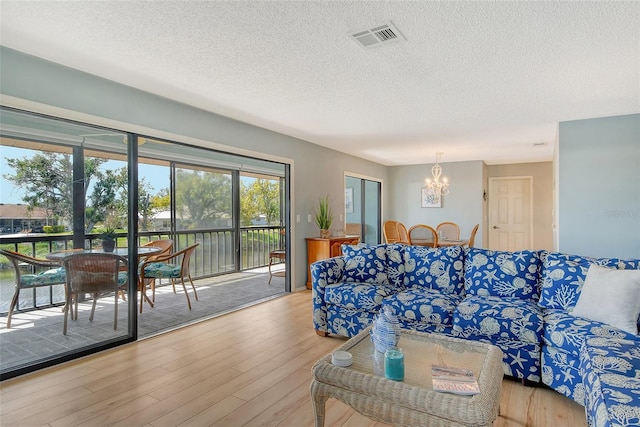 living area featuring a chandelier, a textured ceiling, wood finished floors, and visible vents