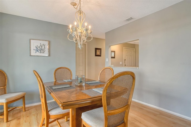 dining area featuring a textured ceiling, a chandelier, visible vents, baseboards, and light wood finished floors