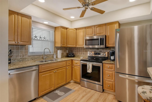 kitchen with light wood finished floors, decorative backsplash, appliances with stainless steel finishes, a sink, and light stone countertops