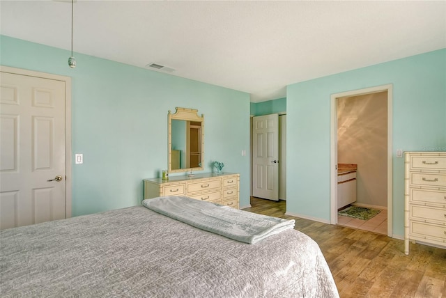 bedroom featuring ensuite bath, wood finished floors, and visible vents