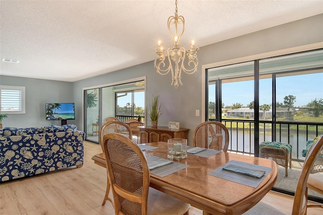 dining space with light wood-type flooring, a healthy amount of sunlight, visible vents, and an inviting chandelier