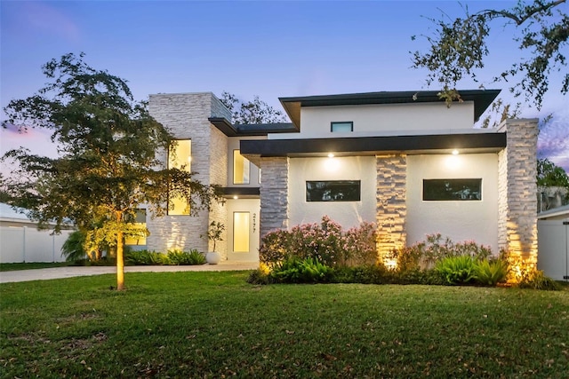 modern home with stone siding, a lawn, fence, and stucco siding