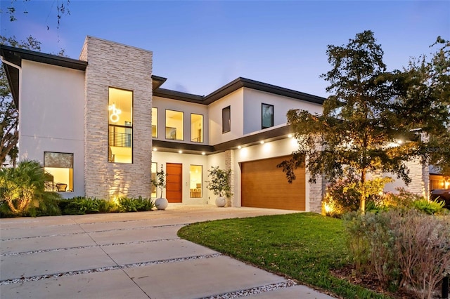 view of front of home featuring driveway, stone siding, an attached garage, a front lawn, and stucco siding