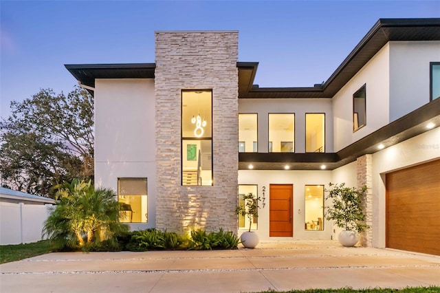 view of front facade featuring a garage, stone siding, fence, and stucco siding