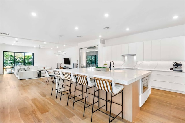 kitchen featuring visible vents, a large island, decorative backsplash, light wood finished floors, and modern cabinets