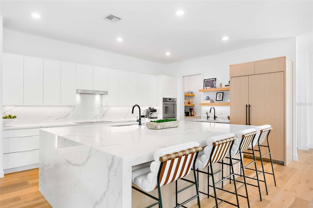 kitchen featuring visible vents, oven, light wood-style floors, open shelves, and a sink