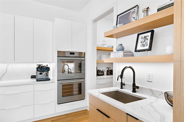 kitchen featuring modern cabinets, light stone countertops, double oven, open shelves, and a sink