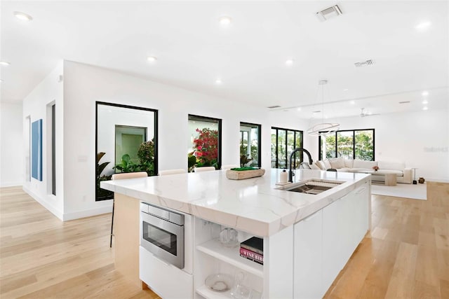 kitchen with a spacious island, a sink, white cabinets, stainless steel microwave, and modern cabinets