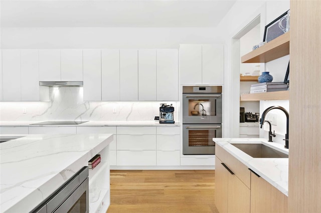 kitchen with modern cabinets, black electric cooktop, double oven, open shelves, and a sink