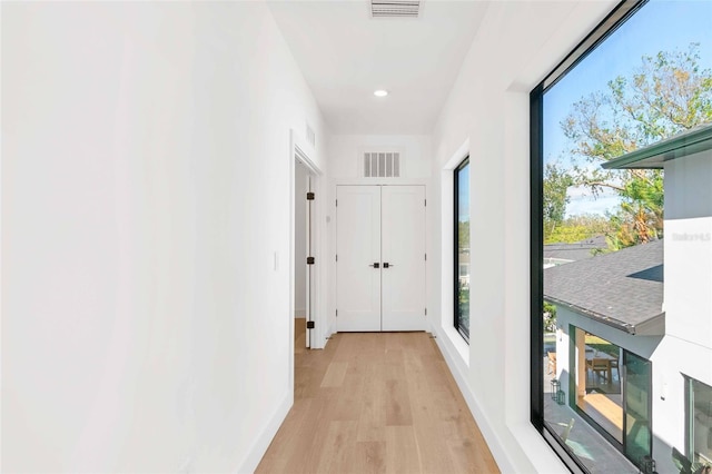 hallway with light wood-style flooring, visible vents, and baseboards