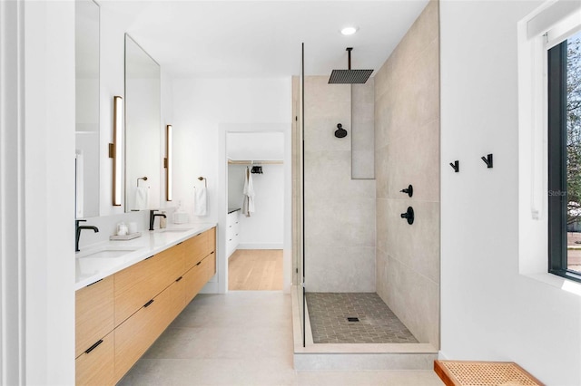 bathroom featuring a tile shower, a sink, and double vanity