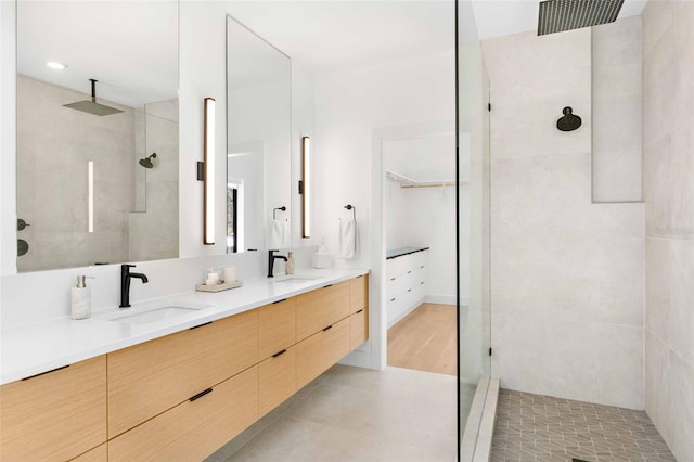 full bath featuring double vanity, a spacious closet, walk in shower, and a sink