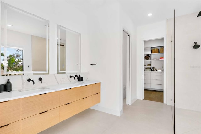 full bath with recessed lighting, a sink, baseboards, double vanity, and a walk in closet