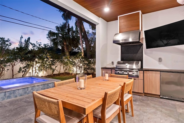 patio terrace at dusk with outdoor dining area, an outdoor hot tub, area for grilling, exterior kitchen, and a fenced backyard