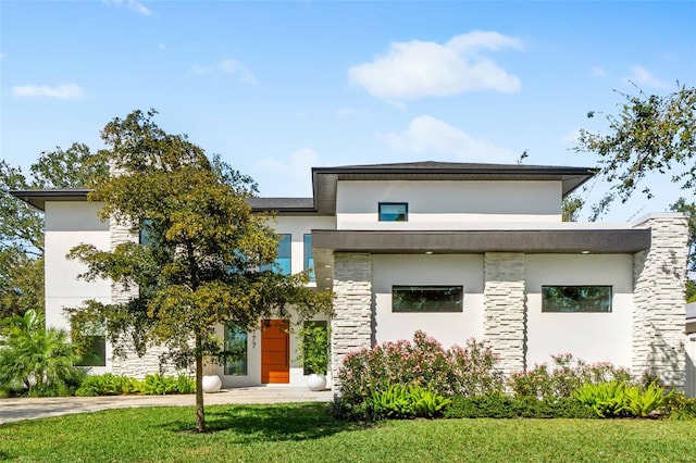 contemporary house featuring stone siding, a front yard, and stucco siding