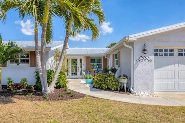 property entrance featuring an attached garage, stucco siding, metal roof, and french doors