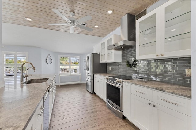 kitchen with stainless steel appliances, a sink, white cabinetry, backsplash, and wall chimney exhaust hood