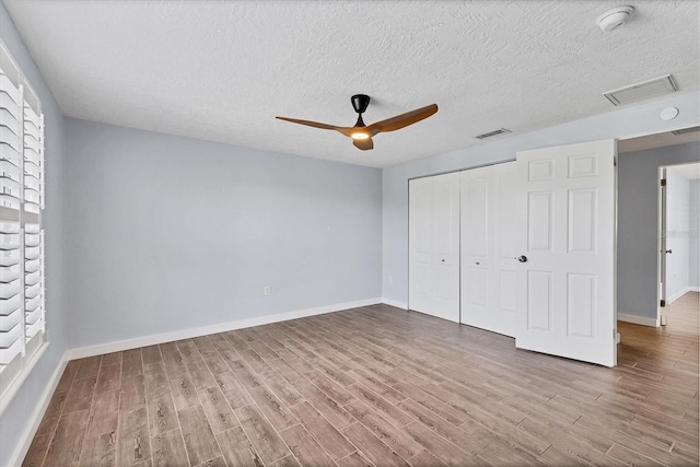 unfurnished bedroom with a closet, wood finished floors, visible vents, and baseboards