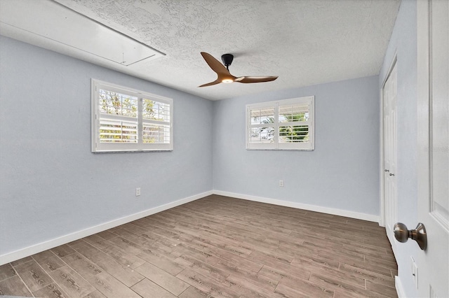 unfurnished bedroom with a textured ceiling, wood finished floors, attic access, and baseboards