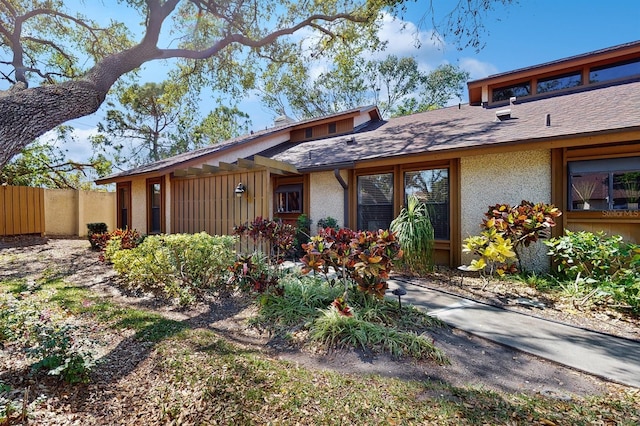 exterior space featuring fence, roof with shingles, and stucco siding