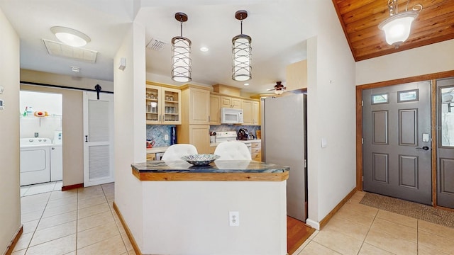 kitchen with white microwave, light tile patterned flooring, freestanding refrigerator, a barn door, and independent washer and dryer