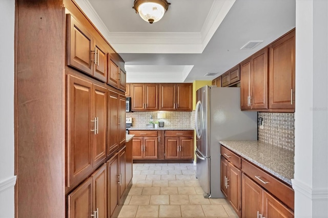 kitchen with visible vents, brown cabinets, freestanding refrigerator, crown molding, and a raised ceiling