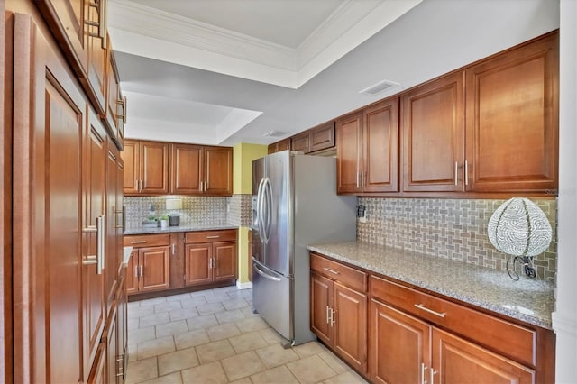 kitchen featuring a tray ceiling, light stone counters, stainless steel fridge, and brown cabinets