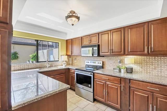 kitchen with a sink, light stone counters, appliances with stainless steel finishes, and brown cabinetry