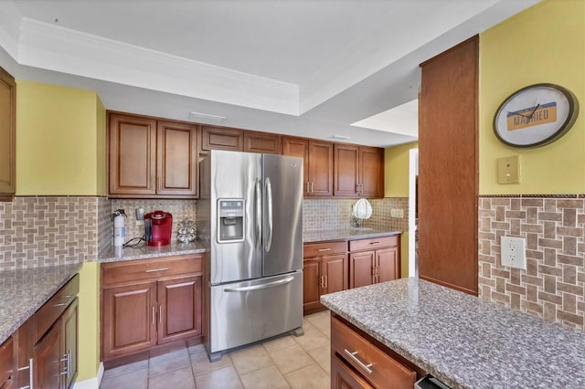 kitchen featuring light stone counters, light tile patterned floors, a tray ceiling, stainless steel fridge with ice dispenser, and tasteful backsplash