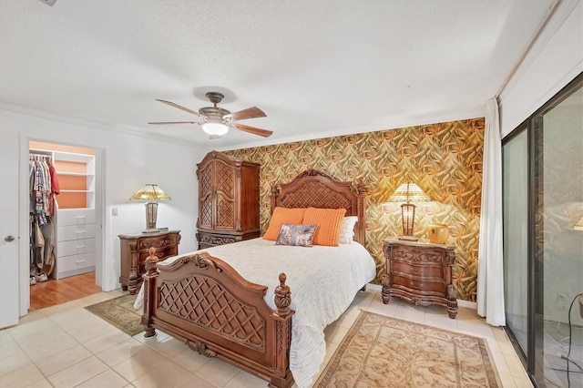 bedroom with wallpapered walls, ceiling fan, a closet, a textured ceiling, and a walk in closet