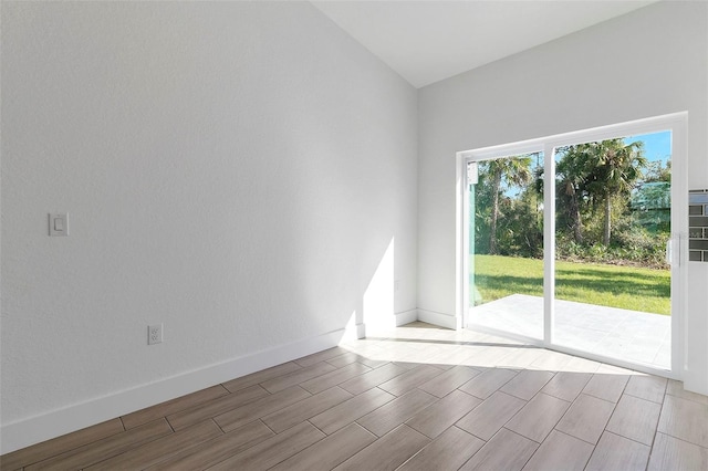 spare room featuring wood finish floors, vaulted ceiling, and baseboards