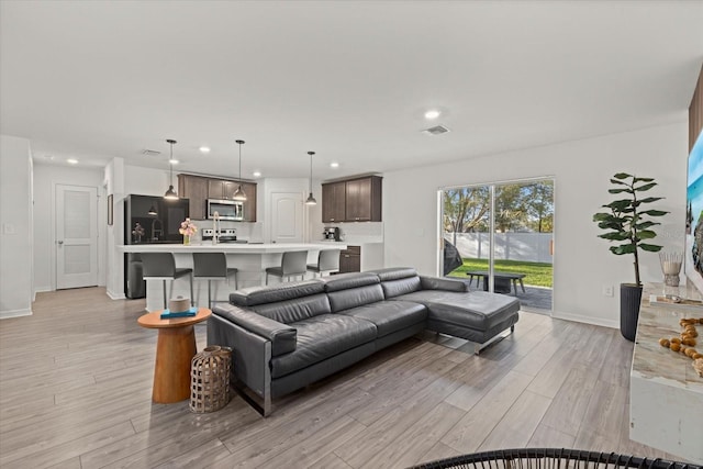 living area featuring baseboards, light wood-type flooring, visible vents, and recessed lighting