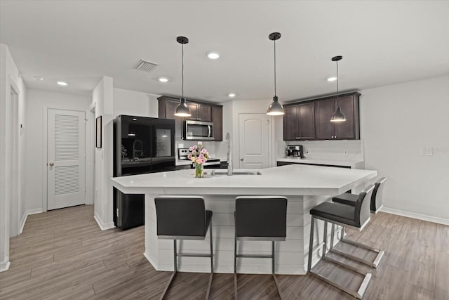 kitchen featuring dark brown cabinetry, visible vents, light countertops, light wood-type flooring, and stainless steel microwave