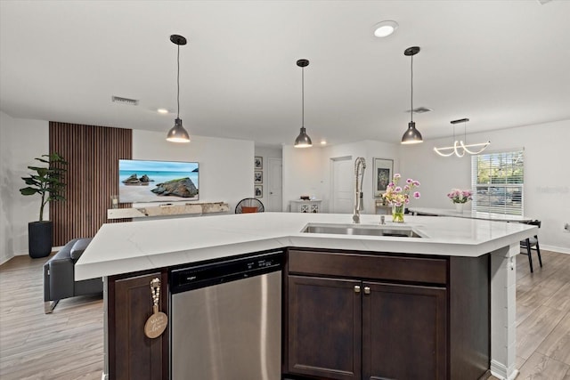 kitchen with light wood-style flooring, dark brown cabinets, hanging light fixtures, dishwasher, and an island with sink