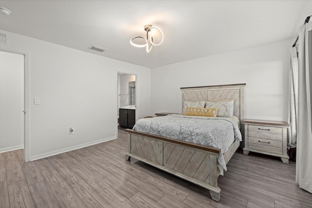 bedroom with visible vents, ensuite bath, baseboards, and wood finished floors