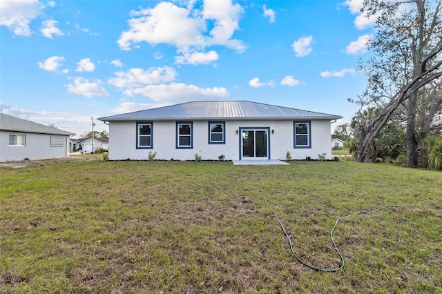 back of property with stucco siding, metal roof, and a yard