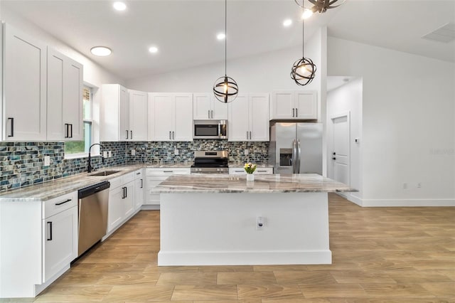 kitchen with a center island, stainless steel appliances, white cabinets, a sink, and light stone countertops