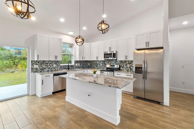 kitchen featuring stainless steel appliances, a kitchen island, a sink, white cabinets, and light stone countertops