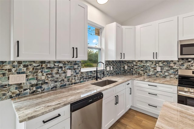 kitchen with lofted ceiling, light stone counters, stainless steel appliances, a sink, and white cabinets