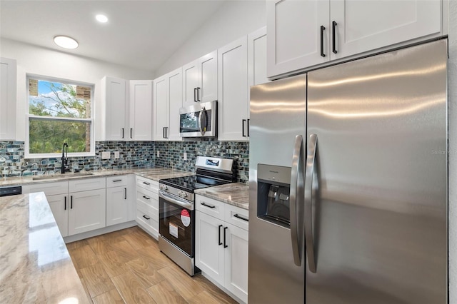 kitchen featuring stainless steel appliances, white cabinets, a sink, and backsplash