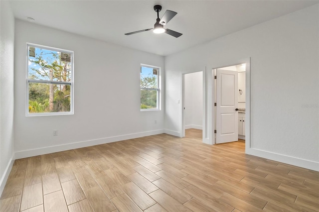 unfurnished bedroom featuring light wood-style flooring, a ceiling fan, baseboards, a walk in closet, and ensuite bath