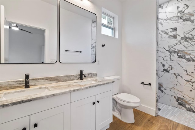 bathroom featuring a sink, a tile shower, toilet, and wood finished floors