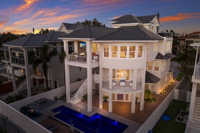 back of house at dusk featuring a standing seam roof, a patio, a fenced backyard, metal roof, and stairs